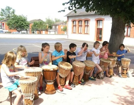 Atelier de percussions africaines : enfants jouant du djembé en cercle dans une cour d’école